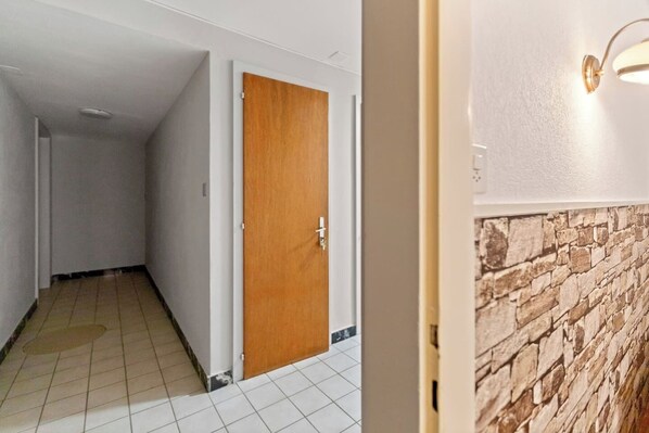 A hallway with a wooden door, white walls, and a tiled floor.