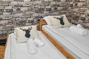 Una habitación con pared de piedra, dos camas con ropa blanca y almohadas con silueta de ciervo.