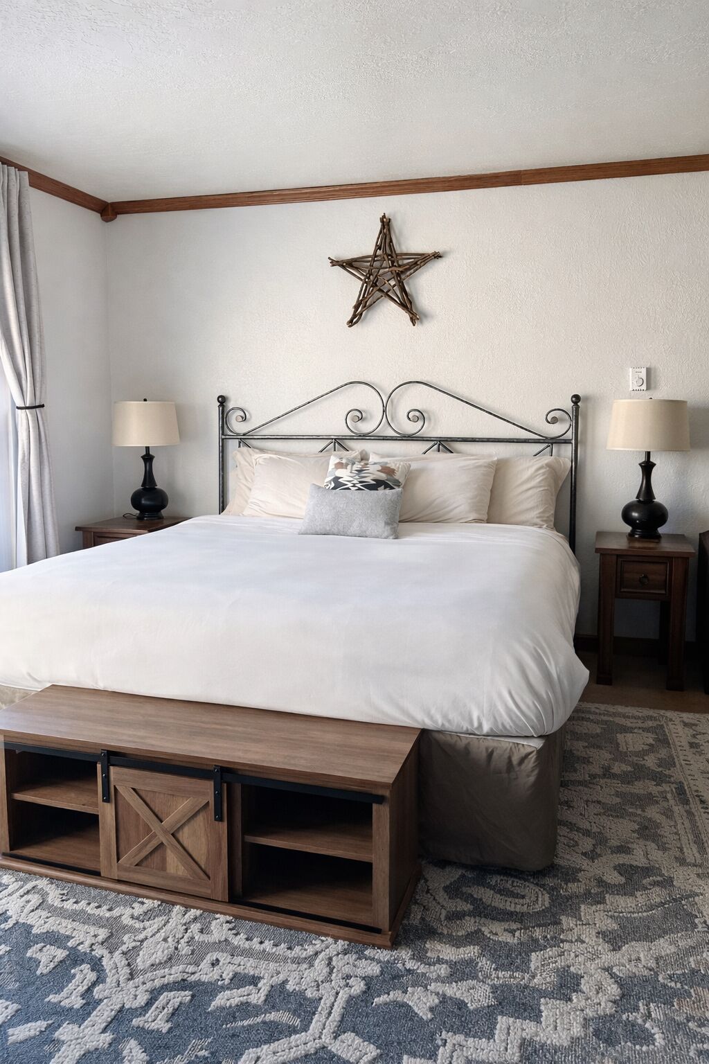 A neatly arranged bedroom with a large bed, two bedside tables with lamps, a star decoration on the wall, and a patterned rug.