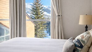 A bedroom with a large bed, a window with curtains, a lamp, and a view of mountains and trees. - Cozy condo with Pool, Jacuzzi, Sauna, & Fitness Center. Minutes to either lift! (Brian Head)