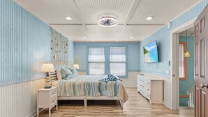 Un dormitorio con cama, mesitas de noche, cómoda y televisor en la pared.