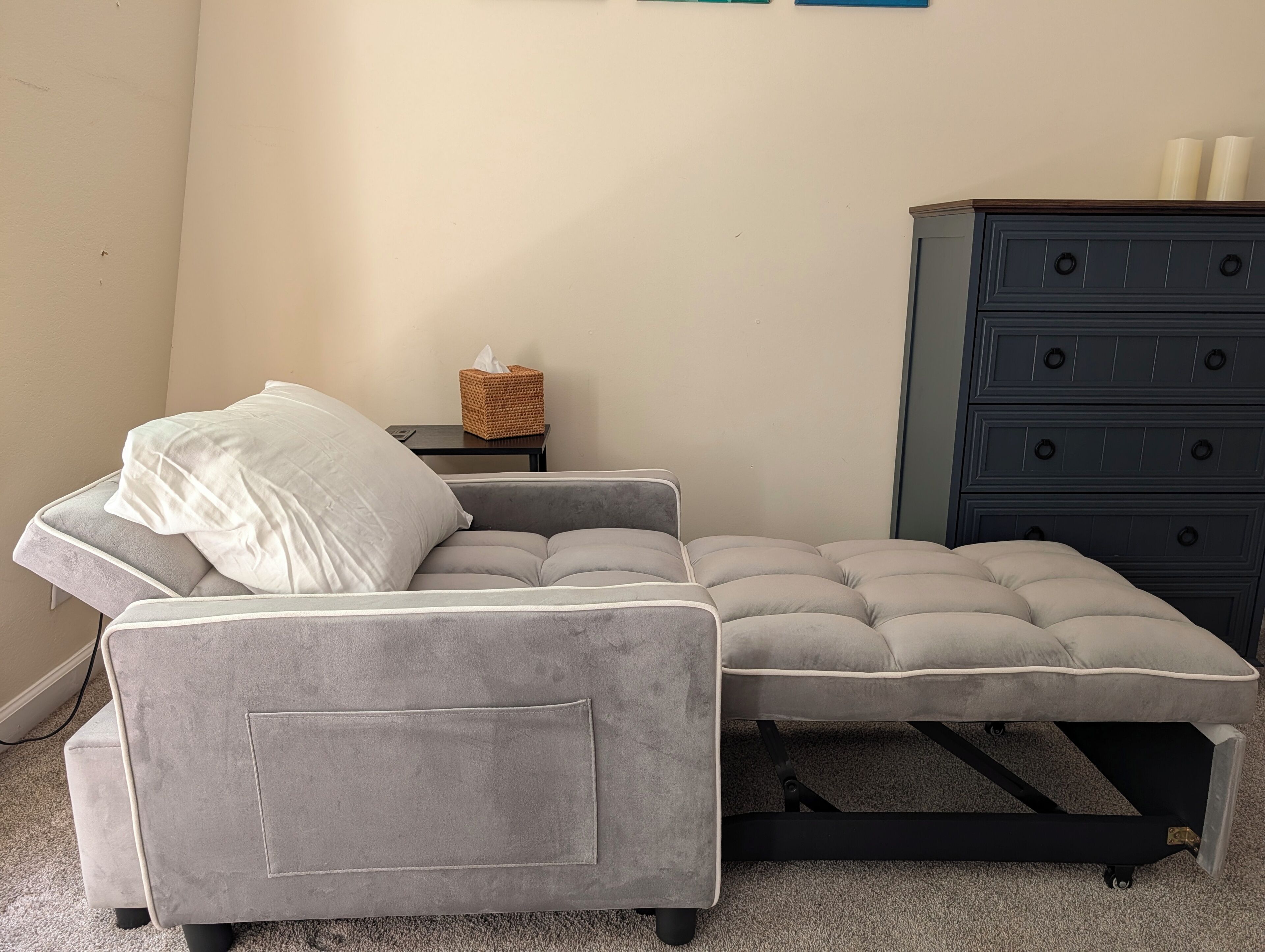 A grey sofa with a cushion, a small side table with a tissue box, and a dark blue dresser with multiple drawers.