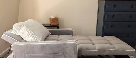 A grey sofa with a cushion, a small side table with a tissue box, and a dark blue dresser with multiple drawers.