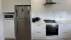 A modern kitchen with a stainless steel refrigerator, a microwave, a gas stove, and a built-in oven. - Cosy and comfortable executive Unit with gorgeous views and close to town centre (Clare)