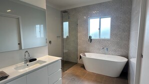 A modern bathroom with a freestanding bathtub, a large mirror, and a shower area. - Cosy and comfortable executive Unit with gorgeous views and close to town centre (Clare)