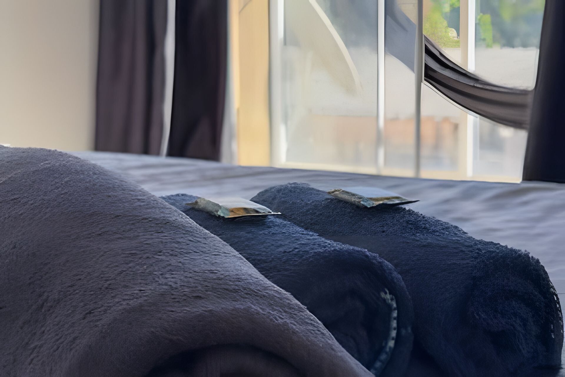 A bed with rolled towels and a window with curtains.