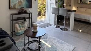 Un'ampia zona giorno con divano, un tavolino rotondo e un quadro appeso al muro. È presente un angolo cottura con tavolo e sedie, e un letto con testiera.