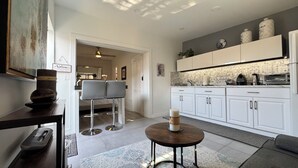 Una cucina moderna con mobili bianchi, forno integrato e macchina da caffè. È presente un'area pranzo con due sgabelli da bar e un piccolo tavolo rotondo.