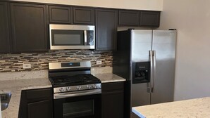 Una cocina moderna con armarios oscuros, un refrigerador de acero inoxidable, un microondas y una estufa a gas.