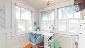 A bright, well-lit room with a desk, chair, and large windows. - Charming Beach Cottage – Walk to Ocean, Relaxing Porch & Private Parking (Carolina Beach)