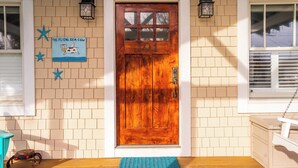 A wooden door with the number 101, a blue mat at the entrance, and a sign with a flying sea cow illustration. - Charming Beach Cottage – Walk to Ocean, Relaxing Porch & Private Parking (Carolina Beach)