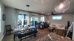 A spacious living area with a dining table, sofas, and a ceiling fan. Large windows provide a view of the outdoors. - Luxurious home with a Gulf View 4-bedroom with a Private Pool on Cape San Blas (Port St. Joe)