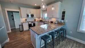 A modern kitchen with white cabinets, a granite countertop, and a central island with bar stools. - Luxurious home with a Gulf View 4-bedroom with a Private Pool on Cape San Blas (Port St. Joe)