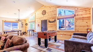 A cozy log cabin interior with a foosball table, leather sofas, and large windows offering views of the outside. - Bearadise ~ Enchanted Dream ~ Mountain Escape (Big Bear Lake)