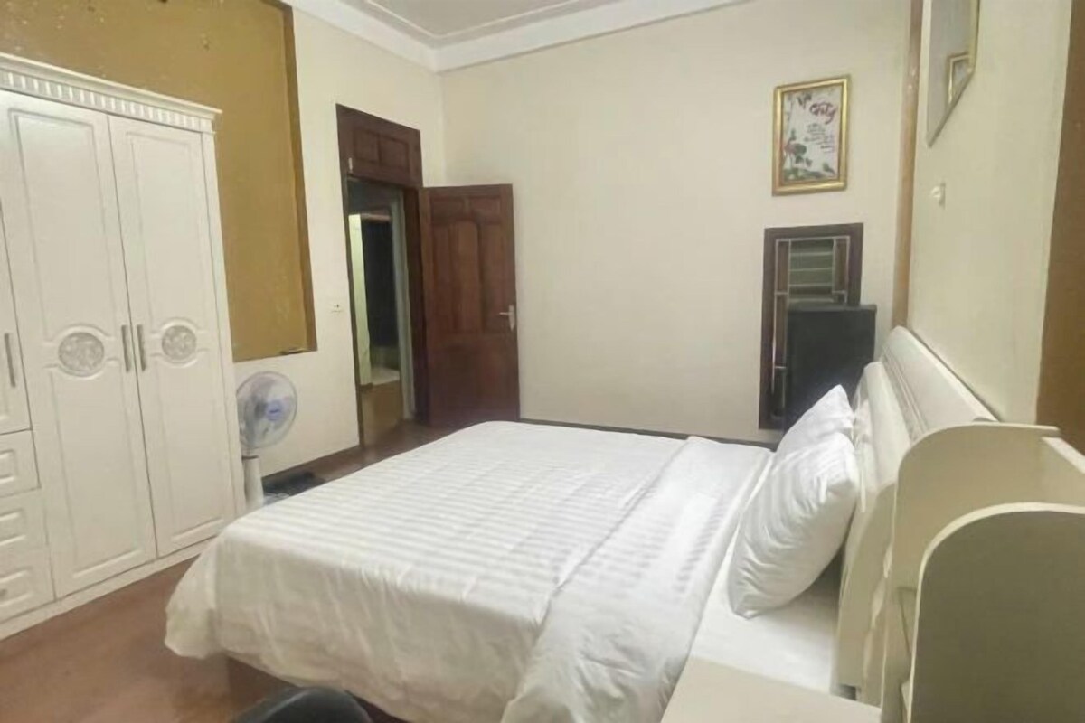 Une chambre à coucher comprenant un lit, une armoire, un ventilateur et une porte donnant sur une autre pièce.