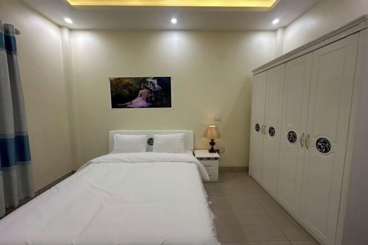 A bedroom with a bed, a nightstand with a lamp, a wardrobe, and a painting on the wall.