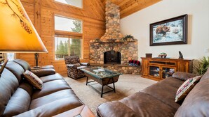 A cozy living room with a stone fireplace, leather sofas, and a large window. - Beautiful log lodge. Bring up to 30 Guests! Snowmobile directly from property!!! (Island Park)