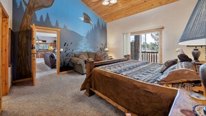 A bedroom with a wooden ceiling, a bed with a brown headboard, a mural of eagles and trees, and a view of the outdoors through a window. - Beautiful log lodge. Bring up to 30 Guests! Snowmobile directly from property!!! (Island Park)