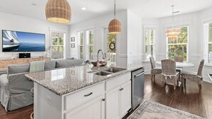 A modern kitchen with a granite countertop, white cabinetry, and a dining area with wicker chairs. - Magnolia Mint | Stylish 4BR Retreat w/ Golf Cart, Bikes, Sleeps 10, Resort Amenities (Santa Rosa Beach)