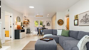 Un salon moderne avec un canapé d’angle gris, une table basse et un coin repas comprenant une table et des chaises.