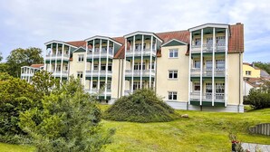 Un hotel de varios pisos con balcones, un césped verde y una pequeña zona ajardinada.