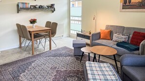 Una sala de estar con un sofá, una mesa de centro, una mesa de comedor con sillas, una alfombra y un cuadro en la pared.