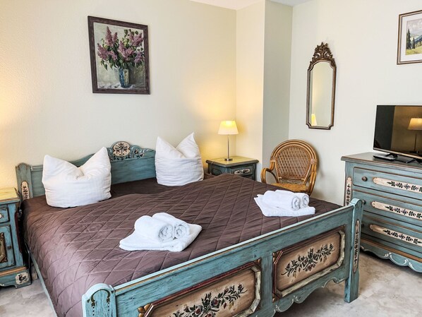 A bedroom with a bed, pillows, a chair, a dresser, a lamp, a mirror, and a painting.