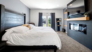Une chambre moderne avec un grand lit, un téléviseur fixé au mur et une cheminée intégrée.