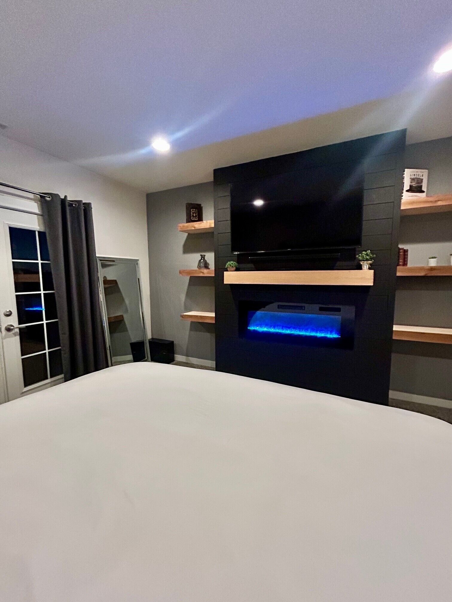 Ein modernes Schlafzimmer mit einem großen Bett, einem an einer schwarzen Wand befestigten Fernseher und Holzböden mit Dekorationselementen.