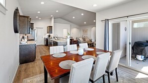 A spacious dining area with a wooden table and chairs, a kitchen in the background, and a sliding glass door leading to an outdoor area. - Game Day Retreat, 4BR w/King Suite, Near Autzen, UofO & Hayward Field. Sleeps 7+ (Springfield)