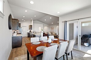 Un vaste espace de salle à manger avec une table et des chaises en bois, une cuisine en arrière-plan et une porte-fenêtre coulissante donnant sur un espace extérieur.