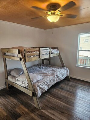 A bunk bed with a ceiling fan in a room with wooden flooring and a window.
