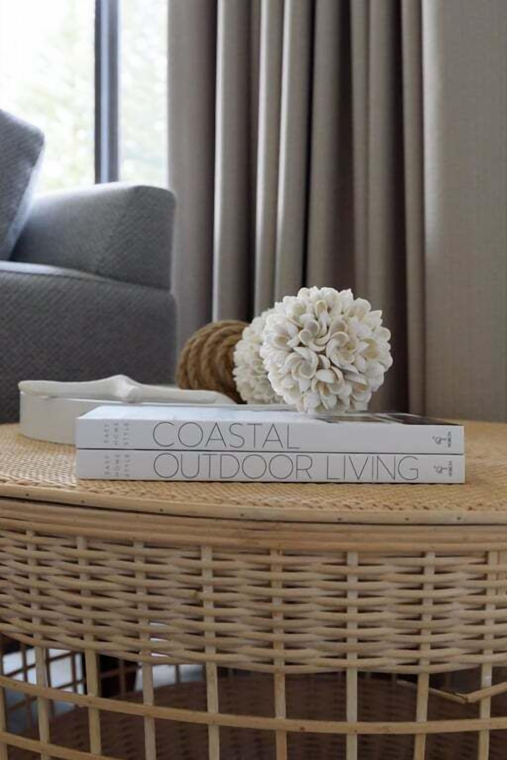 A wicker table with a book titled "Coastal Outdoor Living" and a white floral arrangement.