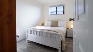 Une chambre à coucher avec un lit blanc, une table de chevet, une fenêtre et une porte.