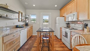A modern kitchen with wooden cabinets, a granite countertop, a central island with stools, a stove, and a refrigerator. - The Cottage on Cherry Lane (Spokane)