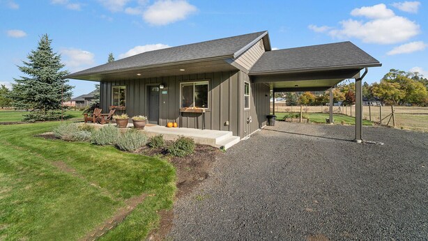 A modern single-story house with a covered patio, a well-maintained lawn, and a gravel driveway. - The Cottage on Cherry Lane (Spokane)