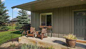 A house with a porch, two wooden chairs, a potted plant, and a window with a view of the yard. - The Cottage on Cherry Lane (Spokane)