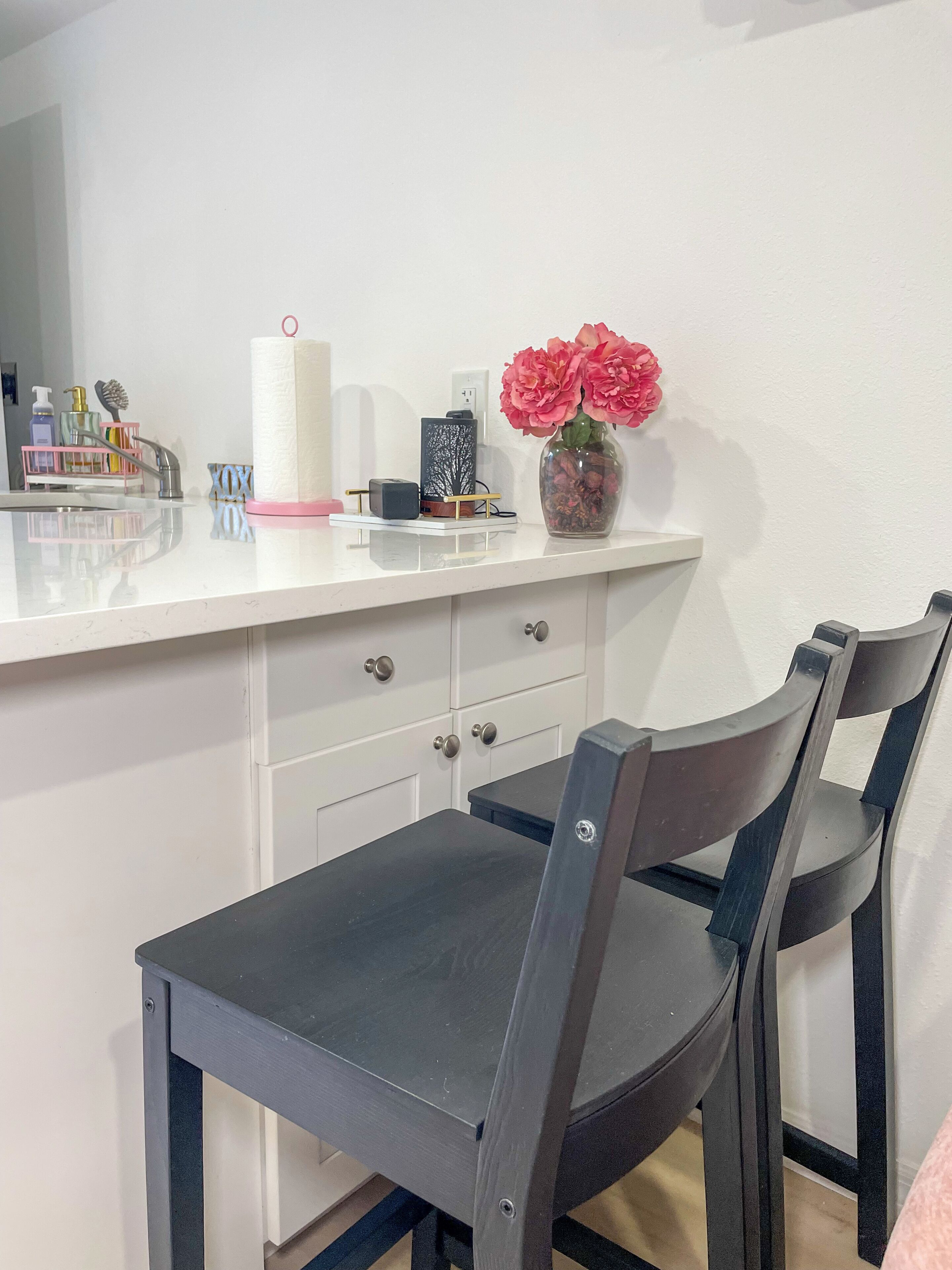 A modern kitchen with white cabinets, a black countertop, and a vase with flowers.