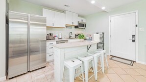 A modern kitchen with white cabinets, stainless steel appliances, and a central island with stools. - Seaside Sanctuary • 2 Min Walk to Okaloosa Beach (Fort Walton Beach)