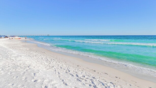 A beach with clear turquoise water, white sand, and a pier in the distance. - Seaside Sanctuary • 2 Min Walk to Okaloosa Beach (Fort Walton Beach)