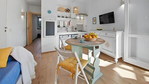 Une cuisine compacte avec des meubles blancs, une table à manger avec des chaises et un téléviseur fixé au mur.