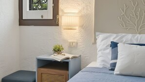 Une chambre à coucher avec un lit, une table de chevet, une lampe et une fenêtre donnant sur un paysage verdoyant.