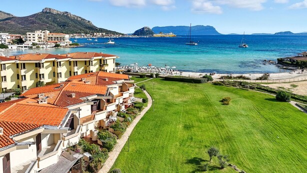 Un hôtel situé sur la côte, composé de plusieurs bâtiments, doté d’une pelouse bien entretenue et offrant une vue sur la mer et les bateaux.
