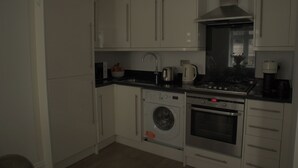 Cocina compacta con armarios blancos, lavadora integrada, horno y estufa.
