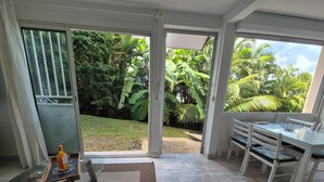 Una habitación moderna con una mesa de vidrio, un sofá blanco y vistas a un jardín exuberante a través de amplios ventanales correderas.