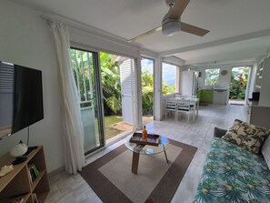 Ein geräumiger Wohnbereich mit Fernseher, Glastisch, Sofa und Deckenventilator.