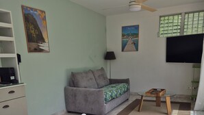 Un salón con sofá, una mesa de comedor con frutero, televisión y obras de arte en las paredes.
