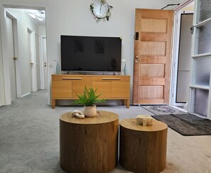 Ein Wohnzimmer mit einem Holz-Fernsehschrank, einem Topfpflanzen und zwei runden Holztischen.