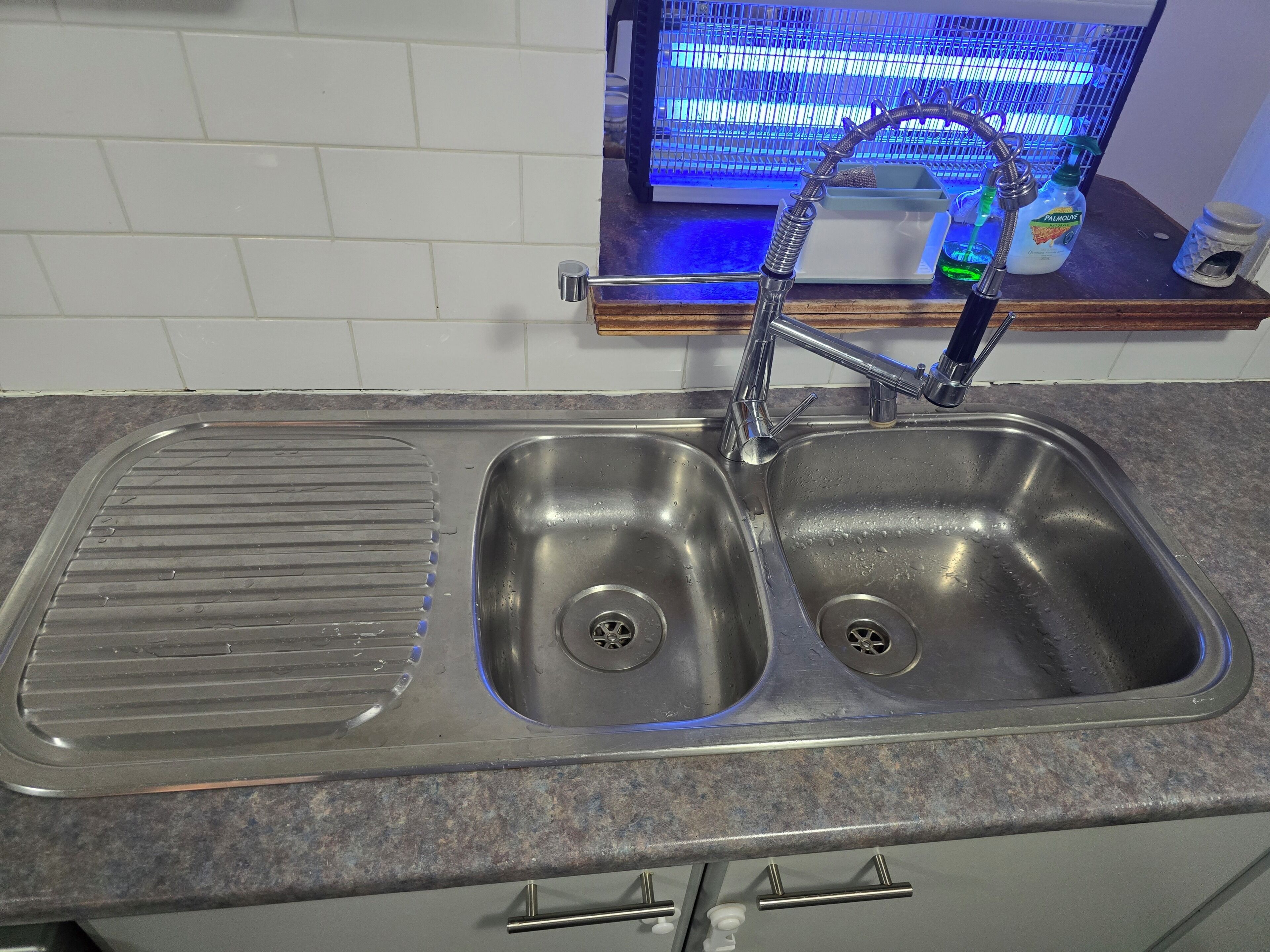 A kitchen with a double stainless steel sink, a built-in grill pan, and a blue lighted aquarium in the background.