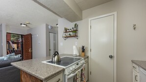 A compact kitchen with a stove, oven, and countertop. There is a door with a handle and a small shelf above it. - 3-Min Walk to Ski Lift | Mountain-View Chalet (Angel Fire)